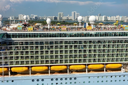 Miami, United States - 16 March 2026: View of a majestic cruise ship's vibrant upper decks teeming with passengers against the gleaming Miami skyline.