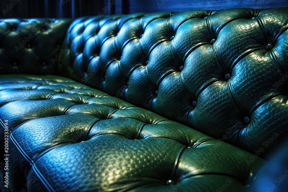 Obraz premium Closeup image of a green tufted leather couch decorated with chainlink texture and vibrant blue illumination