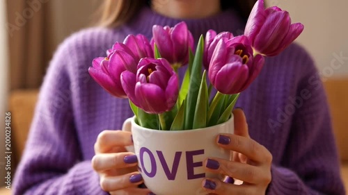 Video for festive design and greetings with close-up woman's hands holding a mug filled with purple tulips and Love text for March 8, Valentine’s Day, Mother’s Day, and birthdays