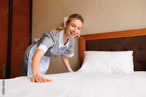 Konstfotografi Female maid smoothing bed sheet while preparing hotel guest room