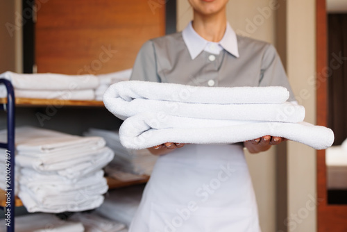 Konstfotografi Hotel housekeeper presenting stack of fresh folded white towels in guest room