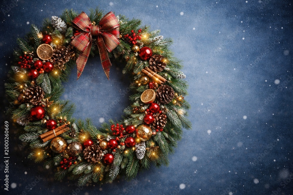 Obraz premium Christmas wreath adorned with mixed synthetic and natural components on blue backdrop with copy space