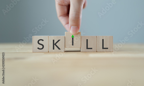 Upskilling and Skill Enhancement Concept. A hand lifts the “I” block in SKILL, forming a gap with an upward arrow, symbolizing upskilling, progress and continuous improvement in workforce capability.