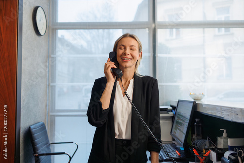 Happy female receptionist answering phone call at hotel reception counter