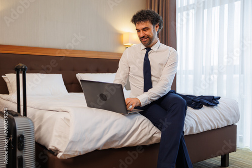 Tableau sur toile Smiling Businessman Working on Laptop While Staying in Modern Hotel Room