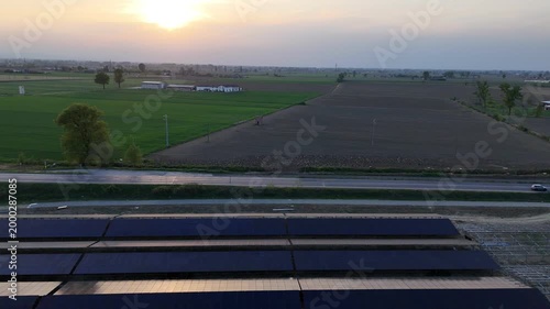Aerial view of a large solar panel installation under construction at sunset, adjacent to agricultural fields and a road in the Po Valley