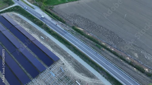 Drone footage captures the expansive construction of a solar power plant in the Po Valley, Italy, adjacent to a busy highway during a picturesque sunset
