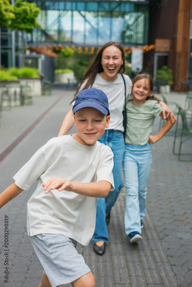 Obraz premium Happy laughing family having fun together outdoors on a casual summer day walking along a city pedestrian street with son in a cap in the foreground