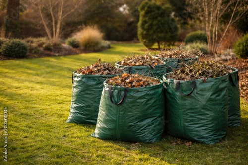 Green bags loaded with leaves and branches for winter garden cleanup on a green lawn area with copy space