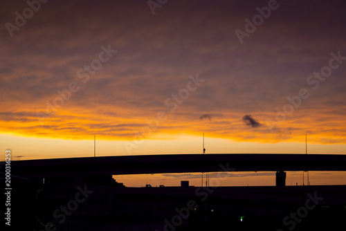 黄金色に染まる夕焼け空と都会の高架橋のシルエット、ドラマチックな黄昏時　Dramatic silhouette of an urban overpass against a golden sunset sky.
