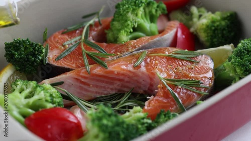 Cooking process. Salmon steak fish seafood with rosemary, broccoli and cherry tomatoes in baking pan. pouring olive oil