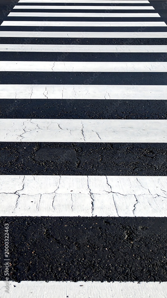 Fototapeta premium A highangle view of a pedestrian crosswalk featuring alternating white paint stripes on weathered asphalt