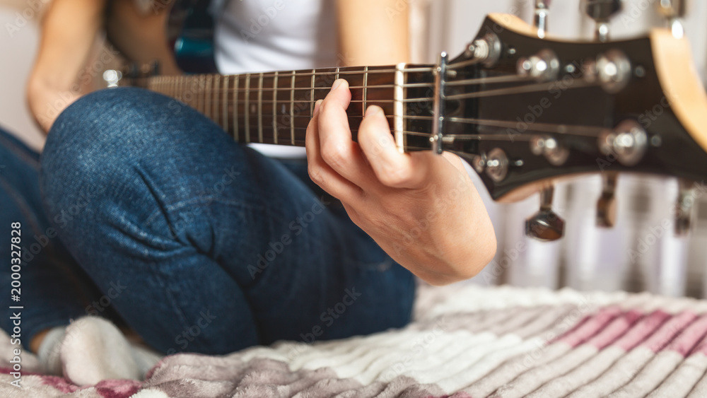 Fototapeta premium Close-up of girl's hands playing electric guitar indoors