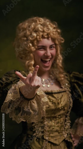 Vertical portrait of Caucasian noblewoman in curly wig and ornate baroque dress laughing while showing middle finger gesture toward camera