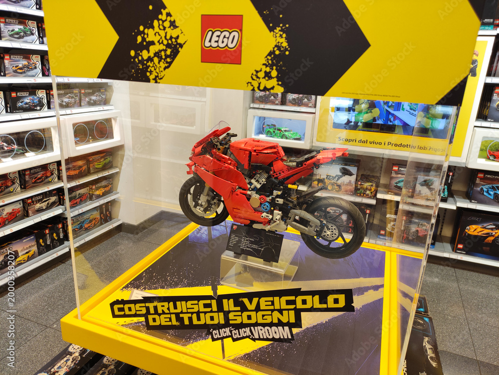 Fototapeta premium Rome, Italy - March 29, 2026: LEGO motorcycle model displayed in a glass case with promotional graphics and colorful shelves of toy sets in the background