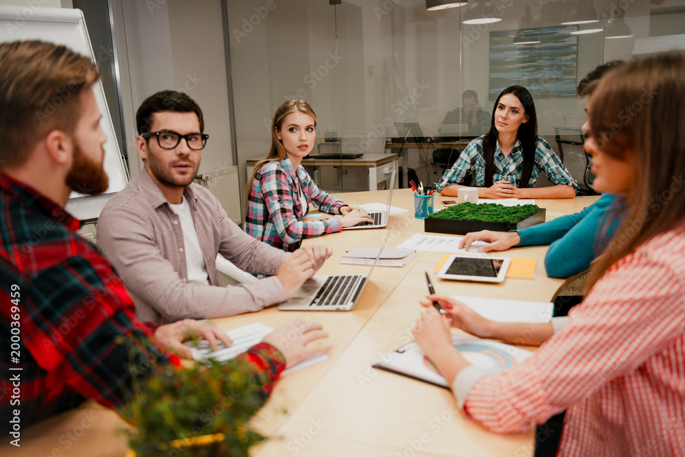 Obraz premium Young team of coworkers having a business meeting around a conference table collaborating on laptops and documents in a modern office