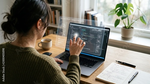 A woman sits at a desk working on a laptop with code displayed on the screen and a transparent overlay of code projected above the keyboard and screen.
