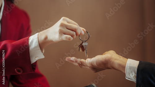 Close-up of a businesswoman handing a house key on a keyring to another person’s open hand, symbolizing real estate transaction, property sale, rental agreement, or home ownership transfer.