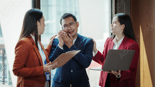 Bilde på lerret Two businesswomen confront a stressed businessman in an office, holding clipboard and laptop, workplace conflict and pressure concept