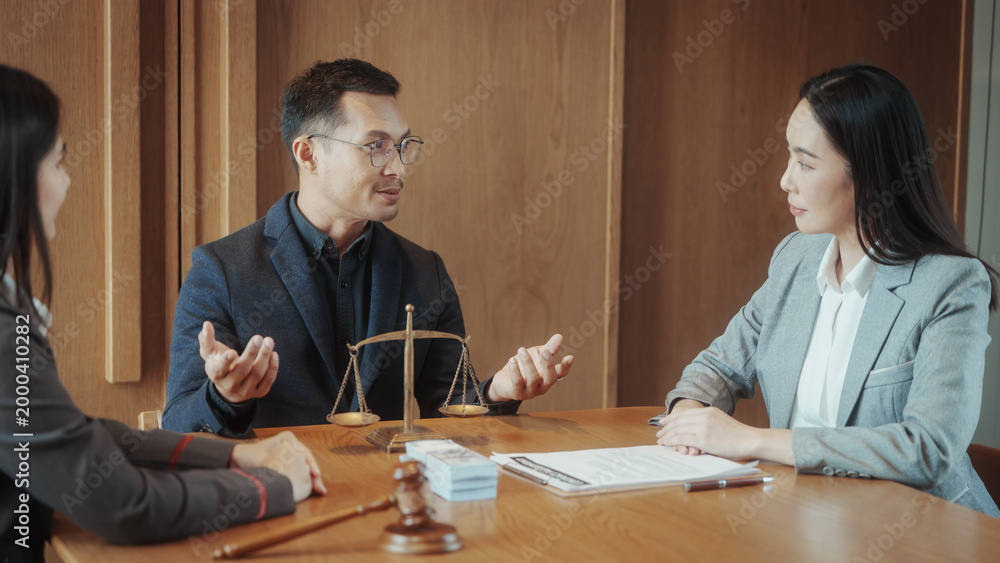 Fototapeta premium Business meeting in lawyer office: man explaining case to two women at wooden table with scales of justice and gavel, professional negotiation and consultation.