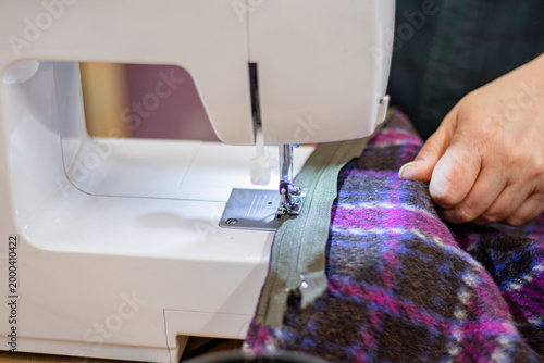 Bild auf Leinwand Sewing machine in use with a person's hand guiding fabric through the presser fo