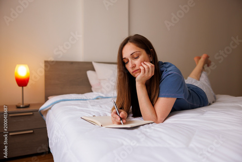 Woman writing in planner making weekly schedule or shopping list in bed after waking up