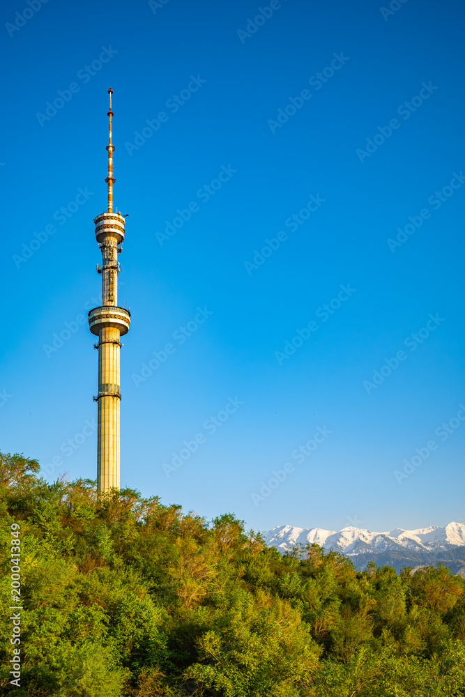 Obraz premium Kok Tobe TV tower landmark against clear blue sky with snow capped Tian Shan mountains in Almaty Kazakhstan