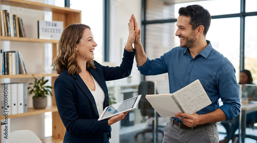 Two happy colleagues celebrating success with a high five in a modern office environment, looking pleased