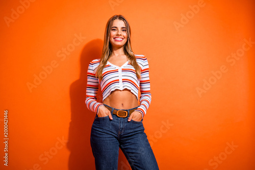 Quadro su tela Young woman in striped crop top and jeans posing against orange background