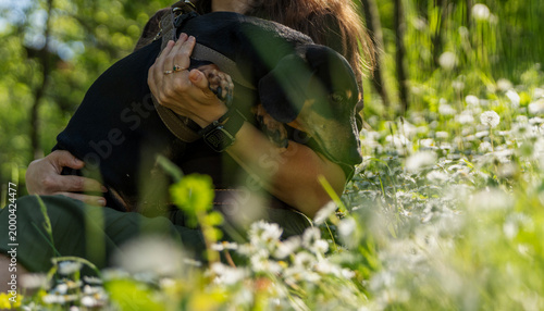 Cuadro en lienzo Happy young woman sitting on green grass and holding cute black dachshund dog in