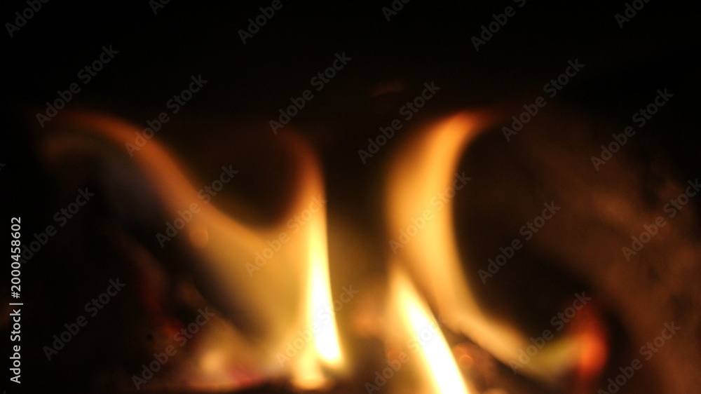Fototapeta premium Wooden logs are burning in the fireplace. Tongues of flame on a dark background. 