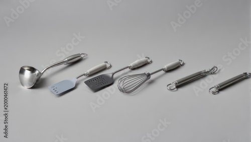 Kitchen utensils, aligned on a neutral surface, showcasing ladle, spatula, whisk, and coils