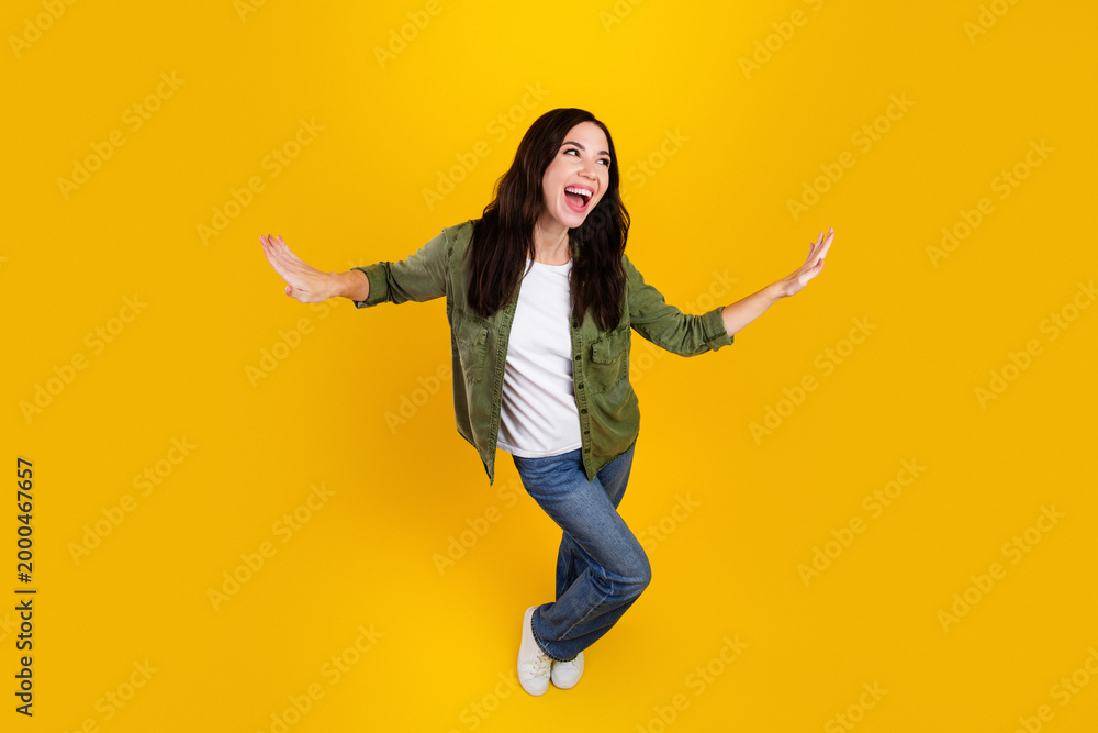 Obraz premium Happy young woman balancing playfully on one foot against a bright yellow background, expressing joy, energy and casual lifestyle