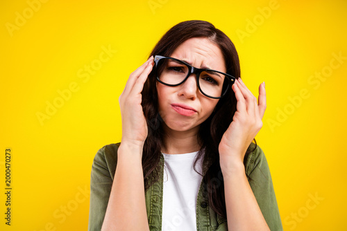 Fotografie Frustrated young woman rubbing temples and adjusting glasses against bright yell