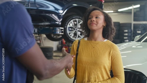 Professional service and customer satisfaction in an auto repair shop, a mechanic shaking hands and returning the car keys to a smiling owner.