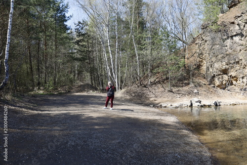 Woman with camera standing by a quarry lake surrounded by trees on a sunny day