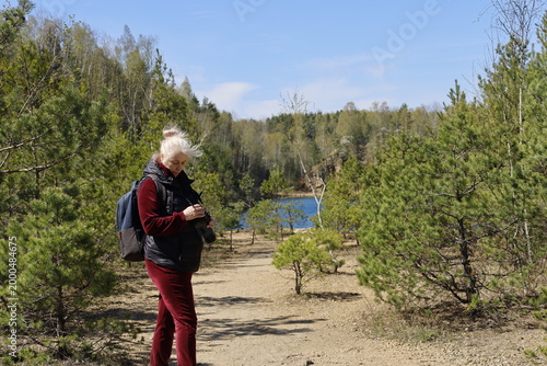 Woman with camera and backpack exploring a scenic forest path near a blue lake