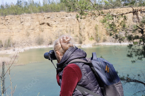 Woman with camera and backpack photographing a scenic quarry lake with rocky cliffs