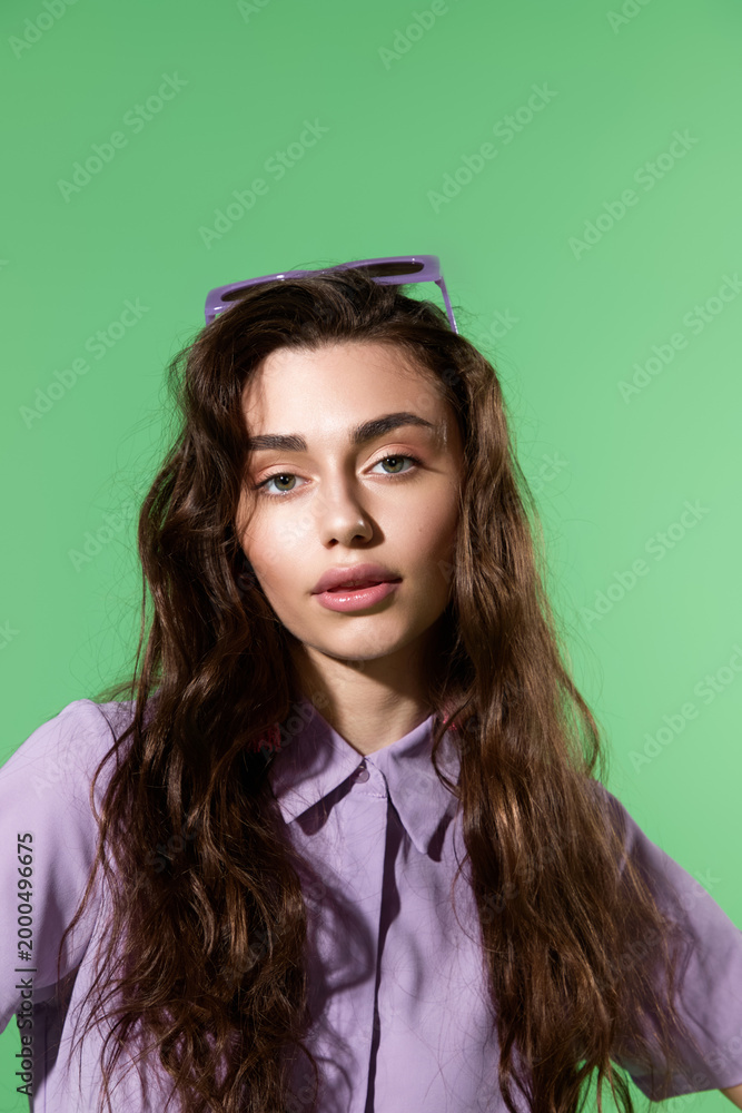 Fototapeta premium Stylish young woman poses confidently against a vibrant green backdrop in modern fashion
