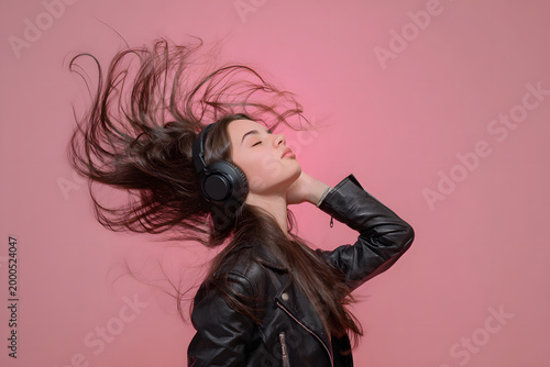 ヘッドホンで音楽を楽しむ女性 髪が舞うダイナミックなライフスタイル、ピンク背景
