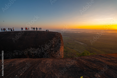 Fotografi A peaceful morning at Three Whale Rock, where visitors gather on rugged cliffs to witness the first light of day