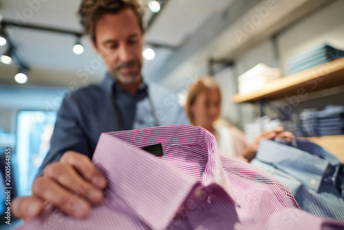 Studio lighting featuring man comparing two shirts while shopping with friend in modern clothing boutique, bright stylish retail interior, clean contemporary design, natural shopping atmosphere, in