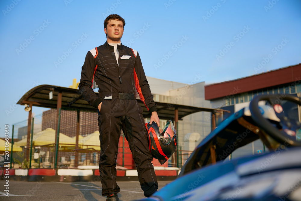 Fototapeta premium A confident young race car driver stands beside a go-kart