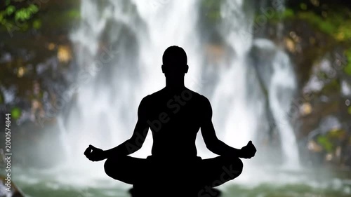 Silhouette of a person meditating in a lotus pose in front of a lush waterfall, symbolizing peace and nature
