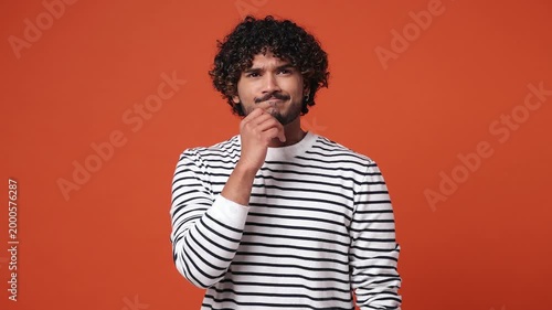 Excited smart puzzled pensive young Indian man wear striped sweatshirt casual clothes look around think scratches at temple comes up with idea raise finger get plan isolated on plain orange background