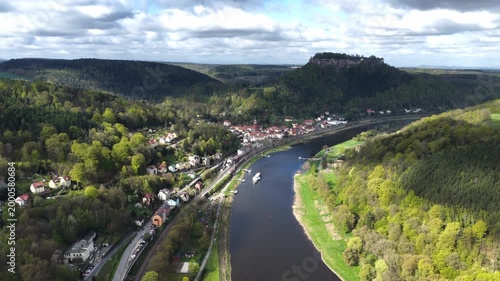 Wide aerial panorama of the Elbe river near Koenigstein in Saxon Switzerland, featuring the fortress, forested valleys, and the town under a dramatic cloudy sky.