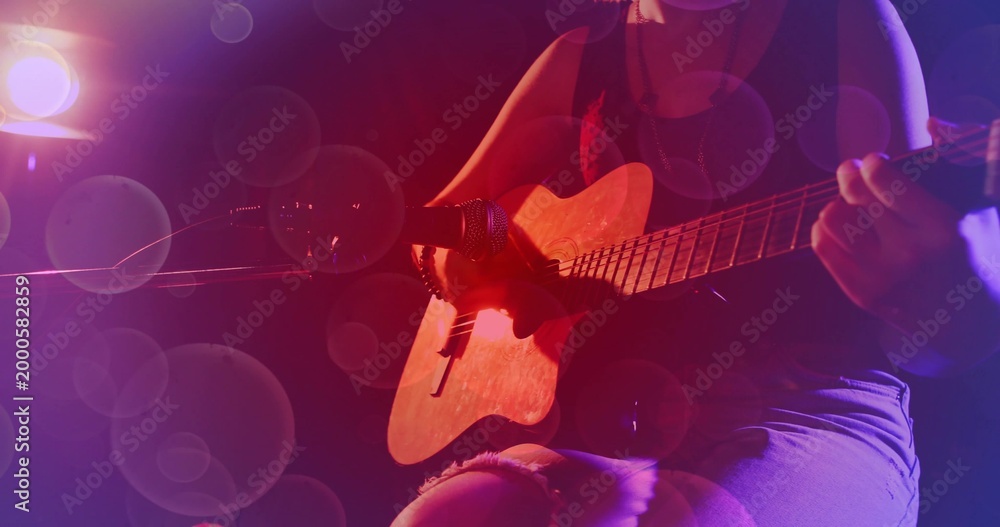 Obraz premium Strumming teen playing acoustic guitar on dim stage, mic stand, red purple lights, ripped shorts