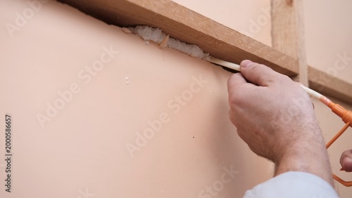 Applying thermal insulation foam with a gun. Using polyurethane foam along wall joints. Expanding the material. Sealing joints and soundproofing walls. Interior renovation. Close-up. Copy space.