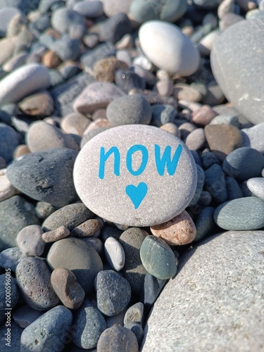 Message on a stone placed among smaller pebbles in a natural setting by a river or beach during a sunny day