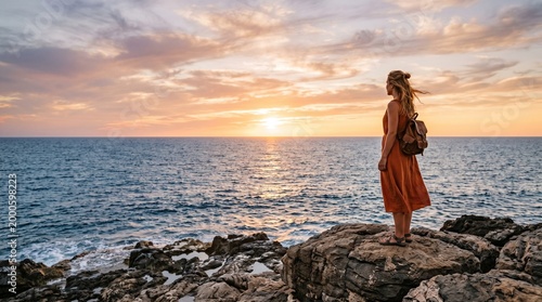 Woman on rocky coast watching sunset over the sea